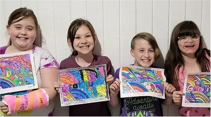 Four smiling children holding colorful rainbow drawings in front of a white wall.