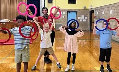 Children and an instructor holding colorful rings in a school gymnasium.