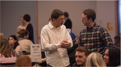 Two men talking amid a seated crowd during an event at Northern Kentucky University.