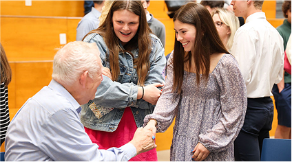 Roger Grein shaking hands with a smiling student as another student looks on and laughs.
