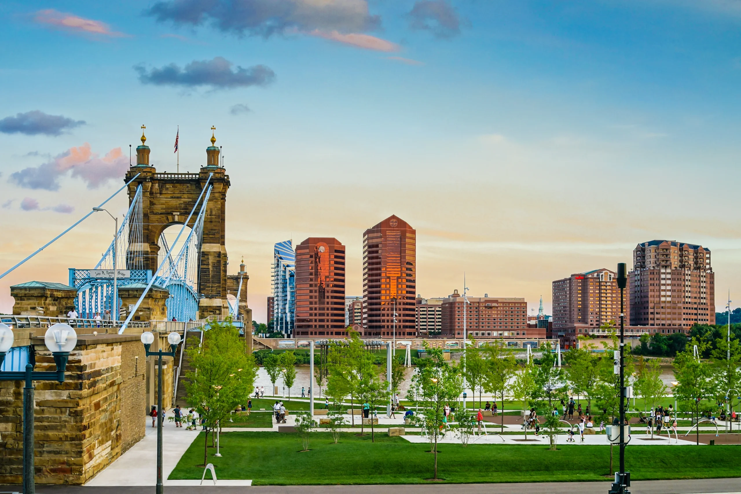 Suspension bridge leading into a cityscape with modern buildings at sunset.